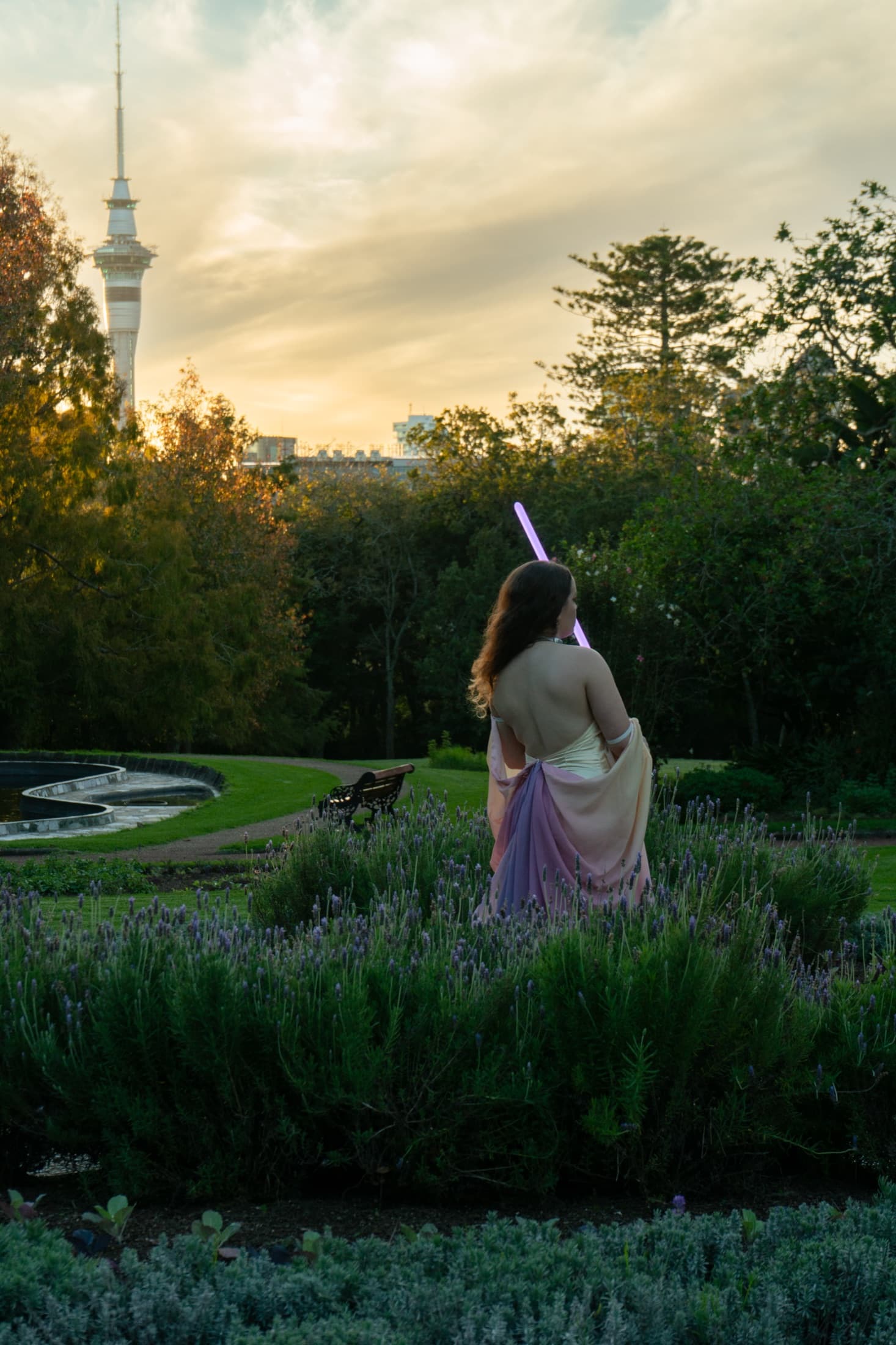 Model standing on a mossy log holding a glowing lightsaber upright at dusk