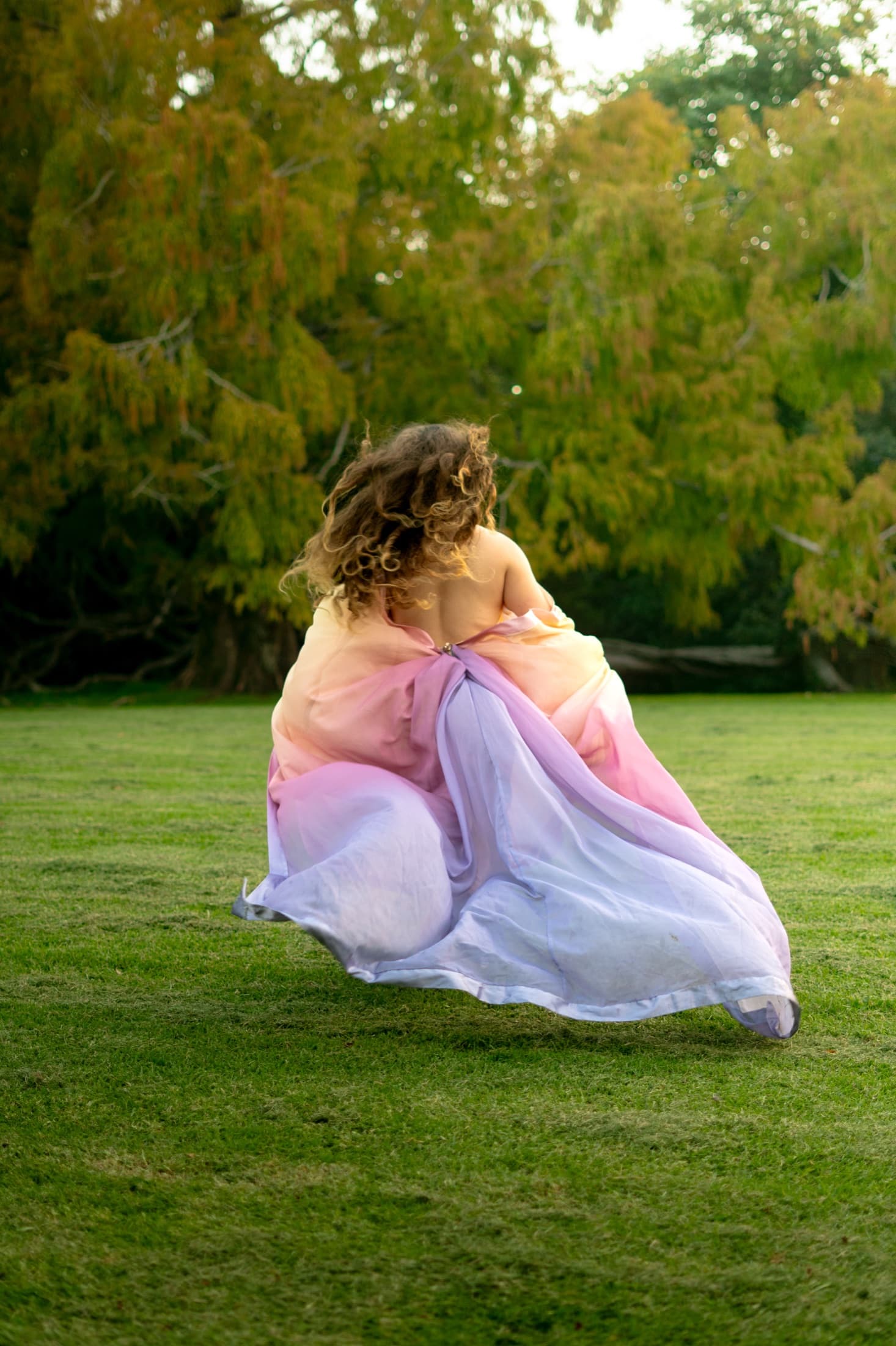 Model in a pastel gown from behind in a garden bed, Sky Tower and sunset sky beyond